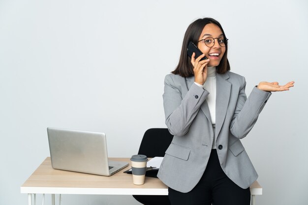 Giovane donna d'affari latina che lavora in un ufficio isolato su sfondo bianco mantenendo una conversazione con il telefono cellulare con qualcuno