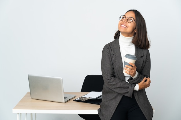 Young latin business woman working in a office isolated on white background looking up while smiling