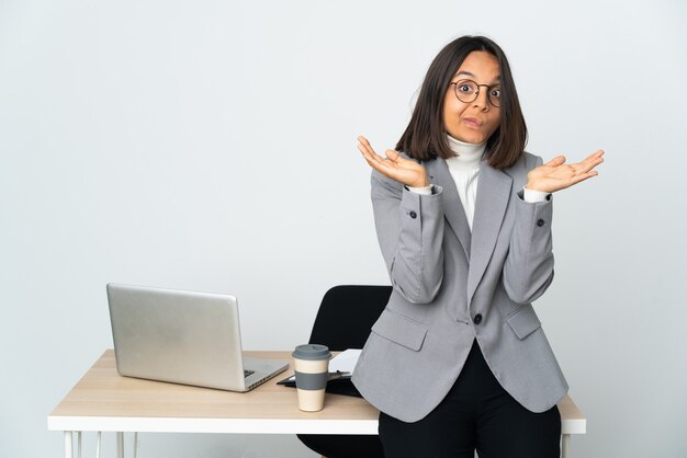 Young latin business woman working in a office isolated on white background making doubts gesture