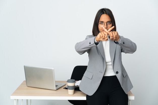 Young latin business woman working in a office isolated on white background making stop gesture with her hand to stop an act