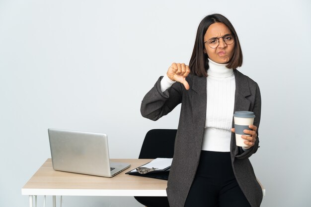 否定的な表現で親指を示す白い背景で隔離のオフィスで働く若いラテンビジネス女性