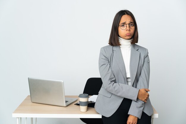 悲しい表情で白い壁に隔離されたオフィスで働く若いラテンビジネス女性