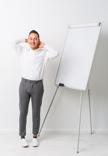 Young latin coaching man with a whiteboard isolated stretching arms, relaxed position.