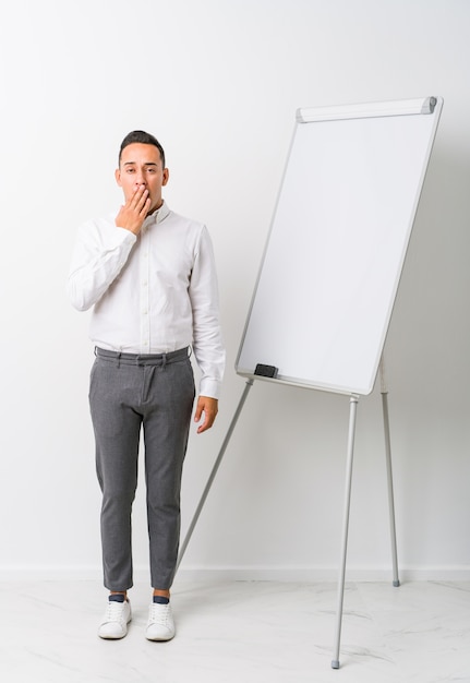 Young latin coaching man with a whiteboard yawning showing a tired gesture covering mouth with hand.