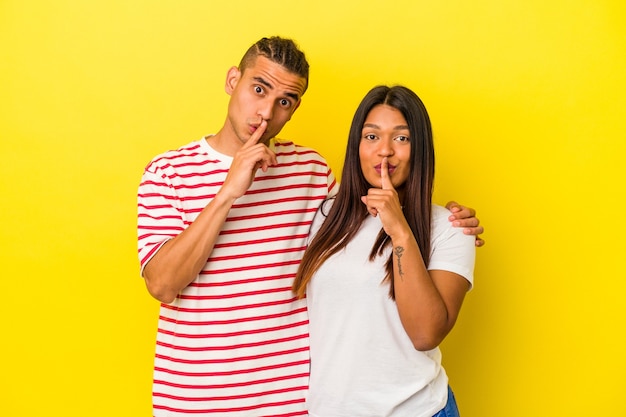 young latin couple isolated on yellow background keeping a secret or asking for silence.