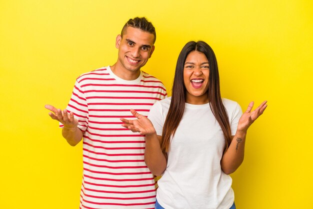 Young latin couple isolated on yellow background receiving a pleasant surprise excited and raising hands