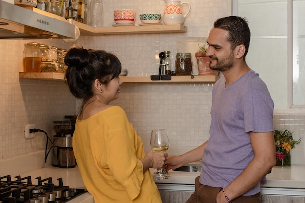 Young latin couple in love holding glasses in house kitchen. Man and woman enjoying free time together