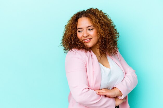 Young latin curvy woman isolated on blue background smiling confident with crossed arms.