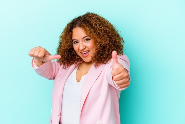 Young latin curvy woman isolated on blue wall raising both thumbs up, smiling and confident.