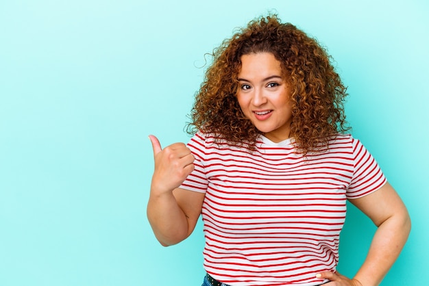 Young latin curvy woman isolated on blue wall shocked pointing with index fingers to a copy space.