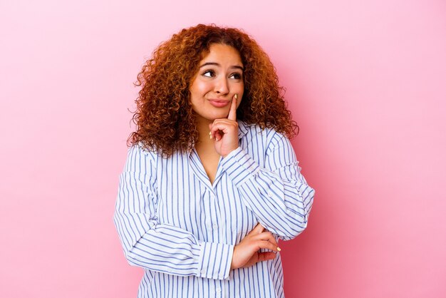 Young latin curvy woman isolated on pink background contemplating, planning a strategy, thinking about the way of a business.