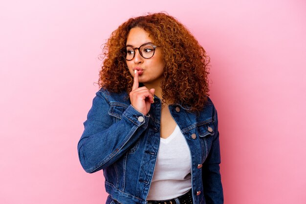 Young latin curvy woman isolated on pink wall keeping a secret or asking for silence.