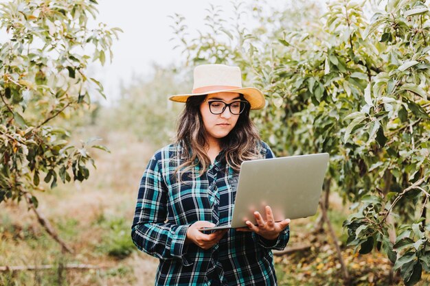 Young latin farmer woman using a laptop to control the production of her farmland