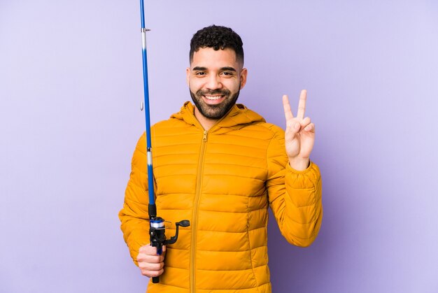 Young latin fisherman holding a rod isolated Young latin fisherman holding a Young latin man playing basket isolated showing number two with fingers.