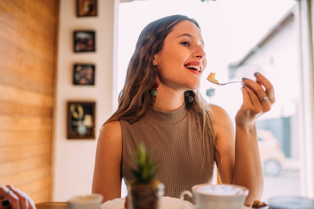 ケーキを食べるカフェに座っている若いラテンの女の子