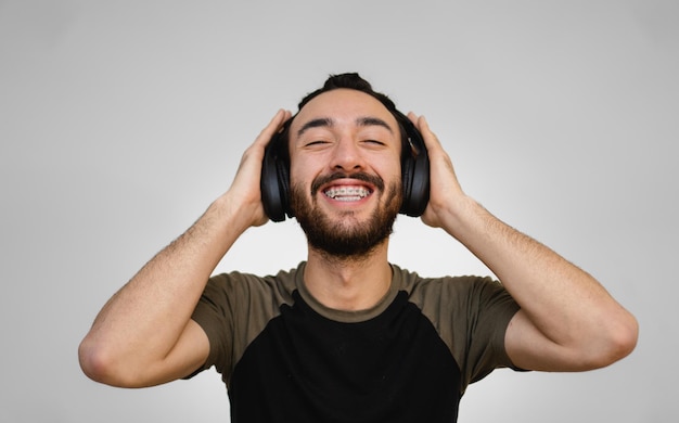 Young latin and hispanic man with braces and beard happy\
listening to music with his eyes closed and a smile on his face\
white background