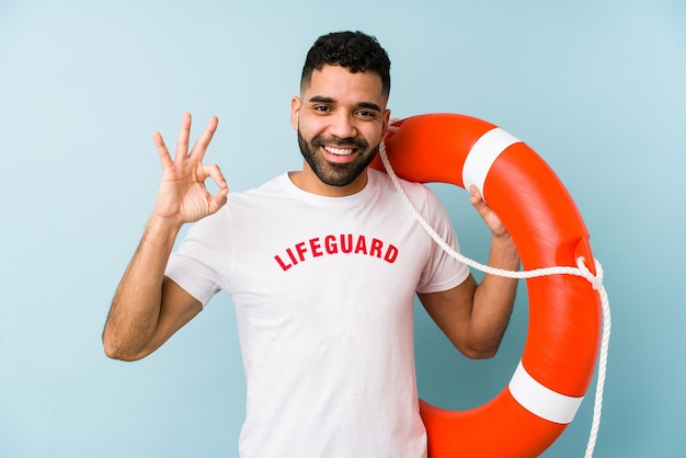 Young latin lifeguard man isolated cheerful and confident showing ok gesture