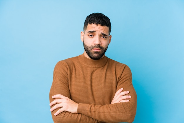 Young latin man against a blue  wall isolated unhappy with sarcastic expression.