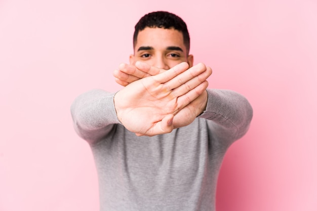 Young latin man against a pink wall isolated doing a denial gesture