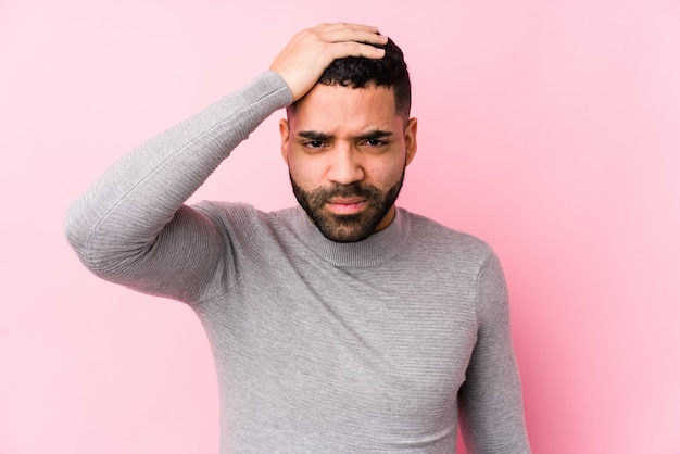 Young latin man against a pink wall tired and very sleepy keeping hand on head.