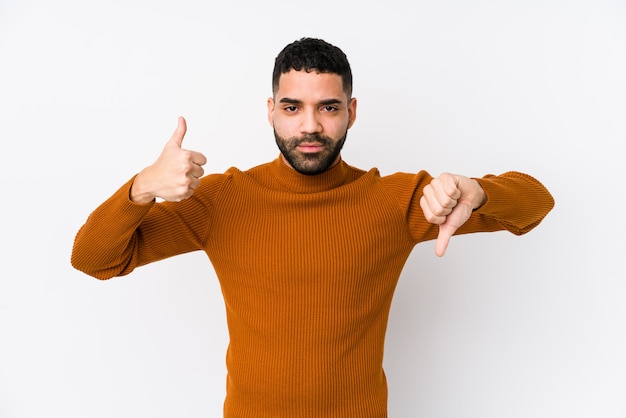 Young latin man against a white wall showing thumbs up and thumbs down