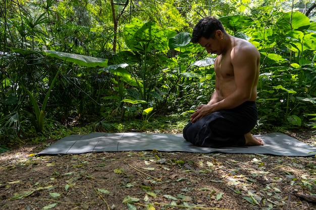 メキシコの自然との平易な直接接触の森の中にヨガマットを配置する若いラテン男