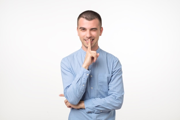 Il giovane latino in camicia blu tiene l'indice sulle labbra cerca di mantenere la cospirazione cerca di mantenere i segreti