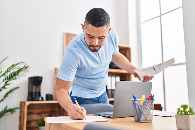 Foto giovane lavoratore d'affari latino che utilizza il computer portatile per scrivere sul documento in ufficio