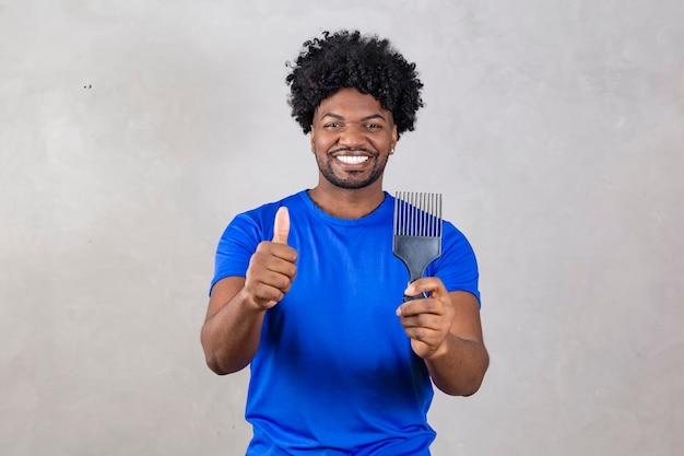 Giovane uomo latino che pettina i capelli forchetta per pettinare i capelli arricciati sfondo grigio