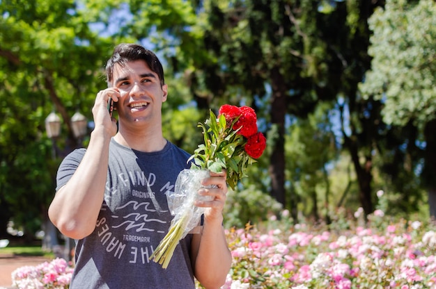 コピースペースで彼のガールフレンドと電話で話している公園で幸せな笑顔の若いラテン系男性