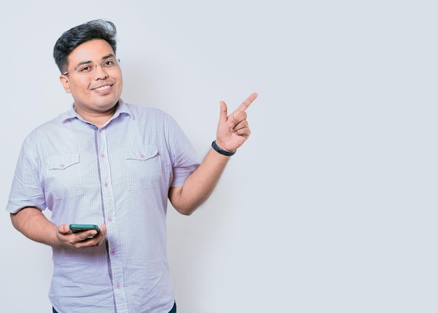 Young latin man holding cellphone pointing to side isolated Happy guy holding cellphone pointing to the side isolated