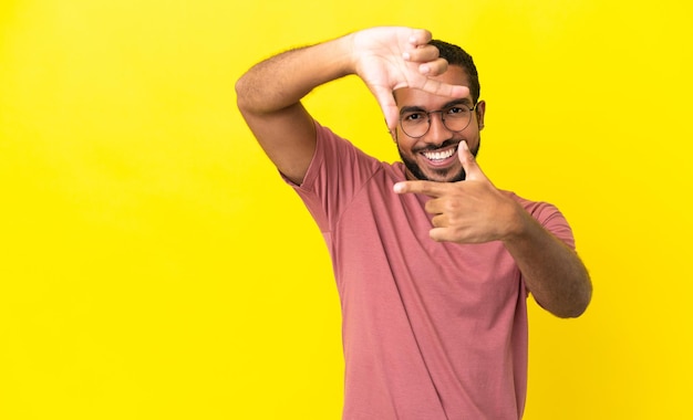 Young latin man isolated on yellow background focusing face Framing symbol