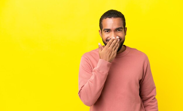 Young latin man isolated on yellow background happy and smiling covering mouth with hand