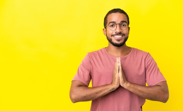 Young latin man isolated on yellow background keeps palm together Person asks for something