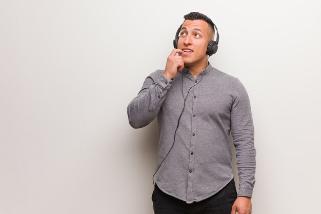 Young latin man listening to music relaxed thinking about something looking at a copy space