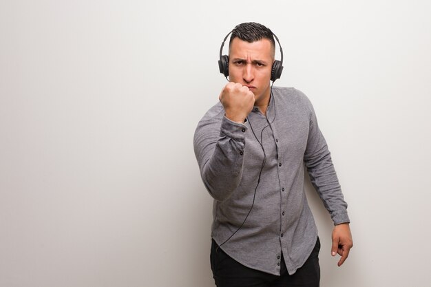 Young latin man listening to music showing fist to front, angry expression