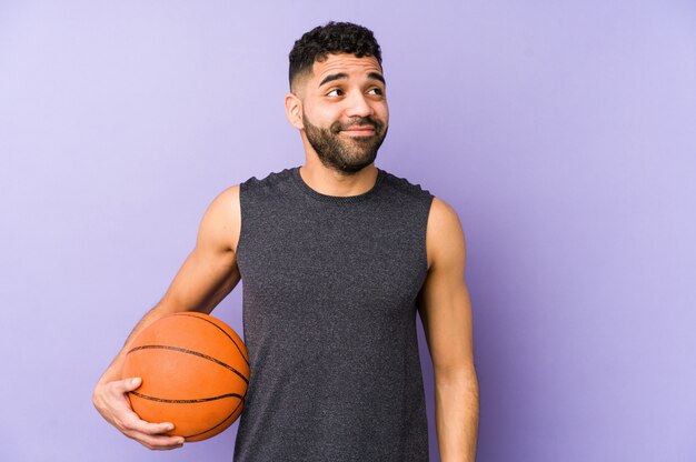 Young latin man playing basket isolated dreaming of achieving goals and purposes