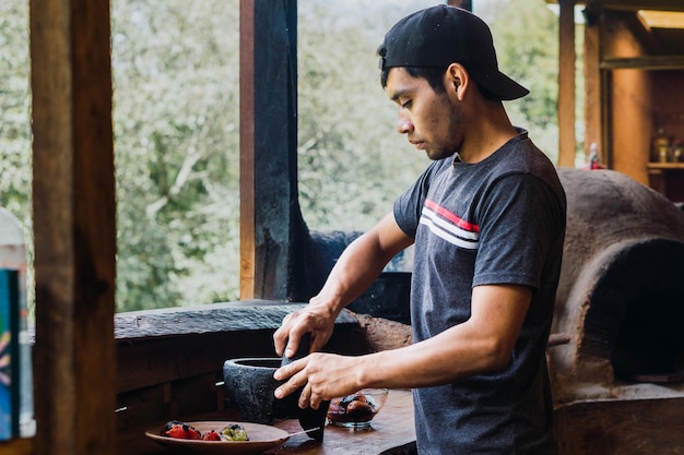 Young Latin man preparing salsa in a molcajete in a traditional kitchen in Chiapas Mexico.