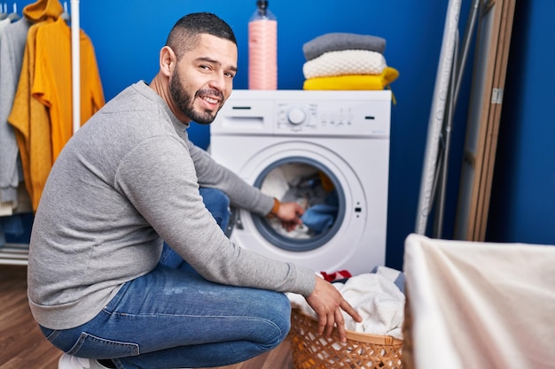 Young latin man smiling confident washing clothes at laundry room