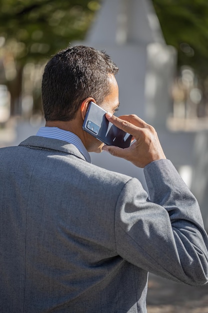 Young latin man in suit walking and talking on mobile phone with copy space