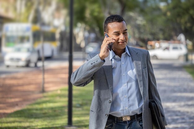 Young latin man in suit walking and talking on mobile phone