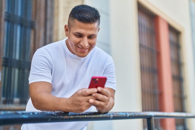 通りの手すりにもたれてスマートフォンを使用している若いラテン男