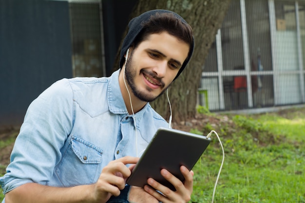 Giovane uomo latino che per mezzo della compressa all'aperto.