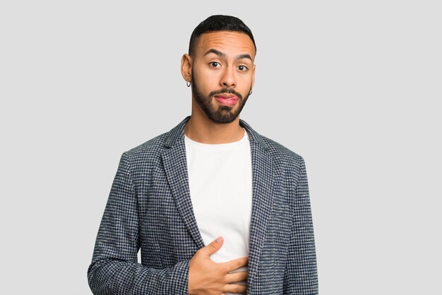 耳輪をかぶったラテン系の若い男 孤立して腹を触り ゆっくりと笑顔で食べる