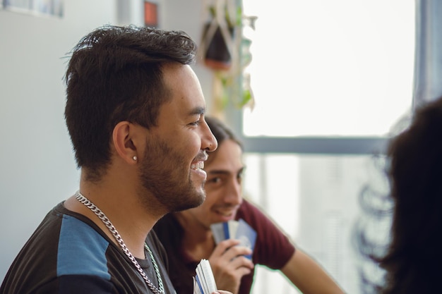 Young latin man with ear piercing smiling while playing cards with friends