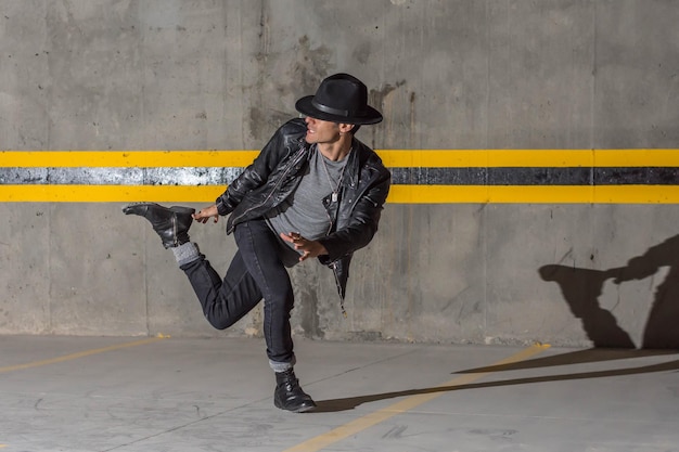 Young latin man with leather jacket, hat and long shadow dancing in underground car parking