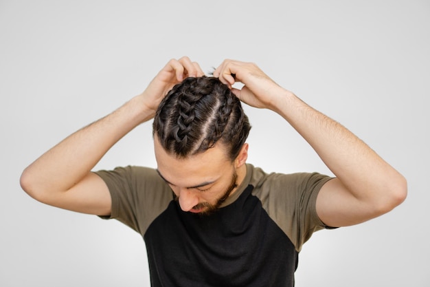 Giovane latino con barba rossa che tesse una treccia lui stesso sfondo bianco