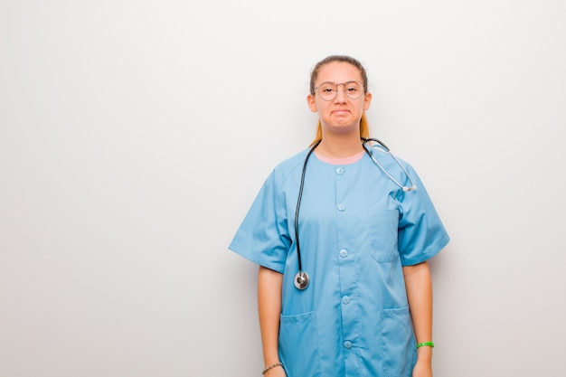 Молодая медсестра-латинка грустит и испытывает стресс, расстроена из-за неприятного сюрприза, с негативным, тревожным взглядом на белой стене