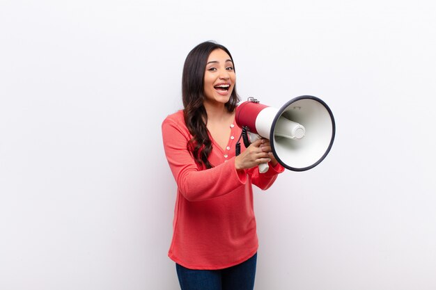 Young latin pretty woman  against flat wall with a megaphone