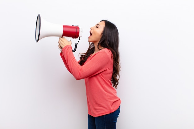 Young latin pretty woman  against flat wall with a megaphone